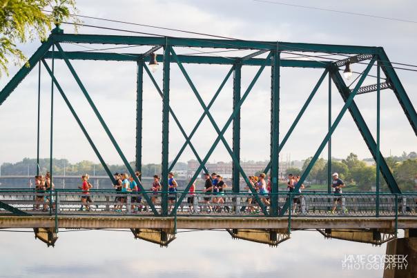 A group of runners running across a bridge that spans a river.