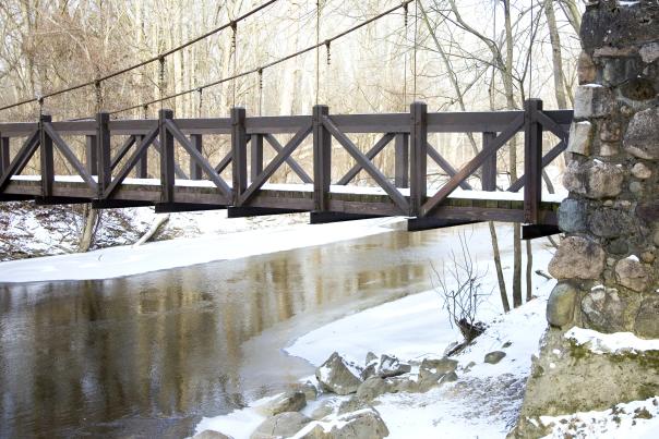 A snow covered suspension bridge over an icy river in Richfield County Park.