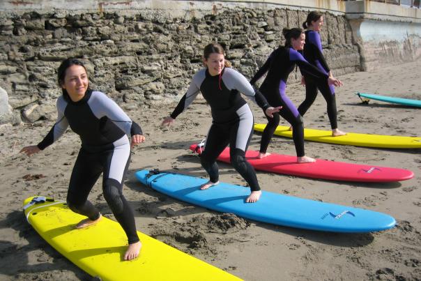 Four learners standing on surfboards in the sand during a lesson with Adventure Out