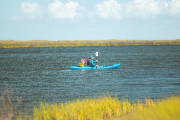 Person wearing hat and blue clothing kayak fishing on calm waters in Corpus Christi, TX with gear