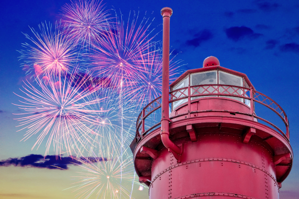red, cylindrical lighthouse tower room is in foreground of 4th of july fireworks