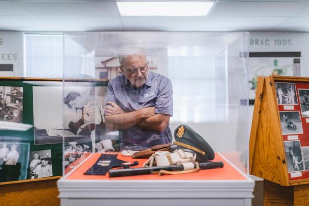 A man peers into a glass box filled with Elvis memorabilia at the Chaffee Barbershop Museum, his arms crossed.