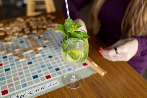A person plays Scrabble with a minty mocktail next to the Scrabble board