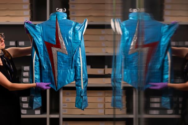 A woman starightens David Bowie's blue jacket with a  red and white lightning symbol on in the archives of the V & A museum in London.