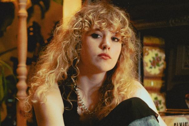 Musician, Fiona-Lee in a black top sits on the floor in a vintage style living room.