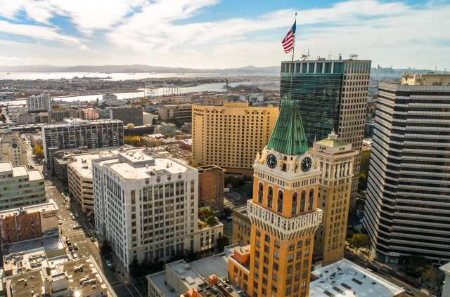 Aerial view of downtown Oakland cityscape with the iconic Tribune Tower, modern skyscrapers, and waterfront.