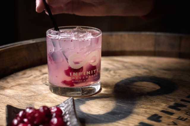 The hand of a person stirring a straw in a pink cocktail at Infinity Beverages Winery & Distillery