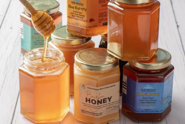 Jars of golden and amber honey are grouped together, with a dipper lifting honey from an open jar.