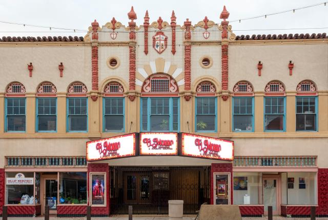 Historic theater facade with Spanish-style architecture, featuring ornate designs, arched windows, and a glowing marquee reading "El Morro" against a twilight sky.