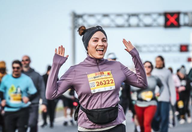 Participant with hands up in purple jacket is excited to be racing at Bay Bridge Run