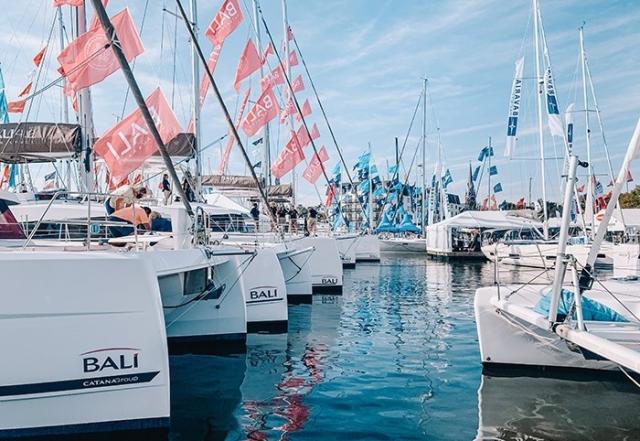 Sailboats and catamarans lined up in the water with flags flying up the mast.