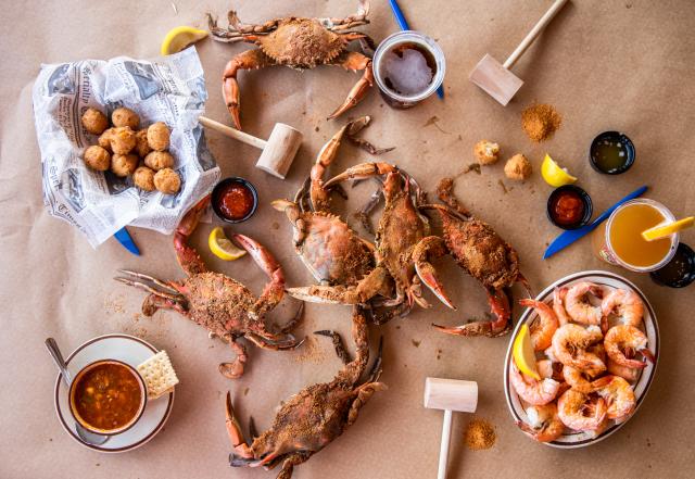 A brown parchment lined table with mallets and steamed crabs, shrimp and hushpuppies on the table.