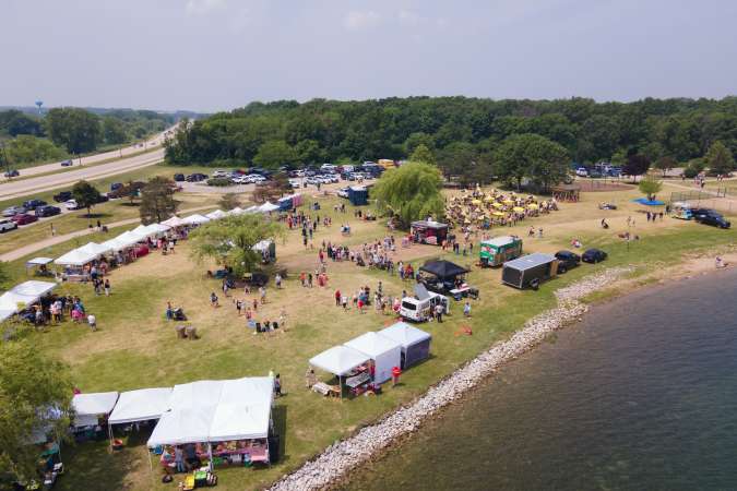 Booths and picnic tables are displayed on the grass, with Lake Andrea shoreline visible nearby.