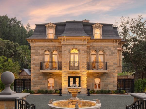 The elegant Francis House mansion has a gabled roof, glowing windows, intricate balconies, and a central fountain, surrounded by lush greenery.