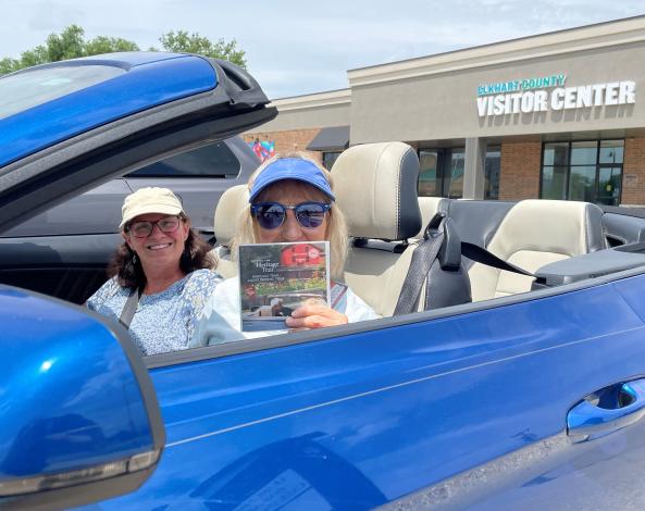 Visitors in a blue convertible holding a Heritage Trail Audio Driving Tour CD