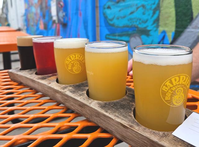 A flight of beers on a table in front of a graffiti wall outside Barrier Brewing Co.
