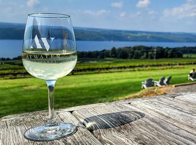 A glass on wine sitting on a wooden boardwalk with views of Seneca Lake in the background