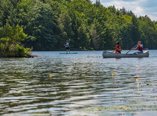 A photo of two people in a canoe and one person paddle boarding on a lake on Noth-South Lake Campground
