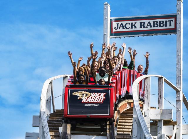 People raise their arms in glee at the first drop on the Jack Rabbit roller coaster at Seabreeze Amusement Park