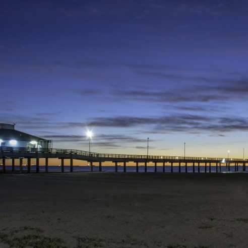 A fishing pier at dawn from the beach perspective as the sun breaks