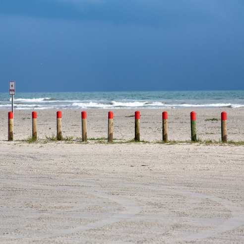 Bollards with a red top in the middle ground with blue water behind and sand in front