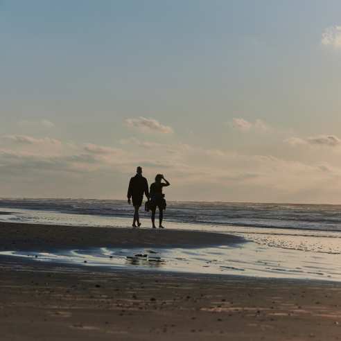 A silhouetted couple walks along the beach