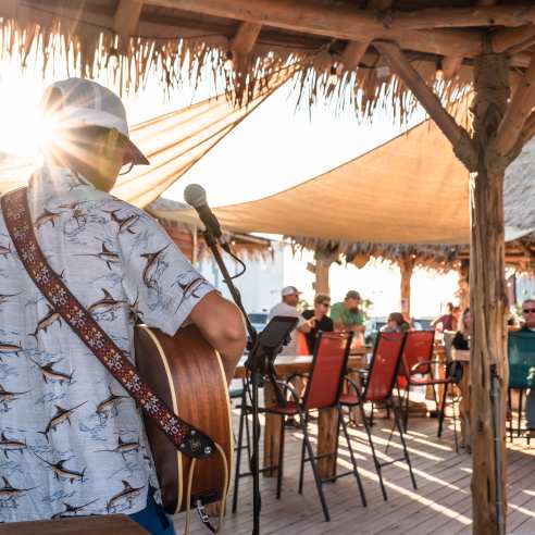 Photo from behind a musician playing guitar towards a tiki bar