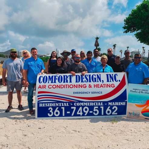 A group of people stand behind and around a large red, white, and blue sign reading "Comfort Design, Inc" with other details of the business below.
