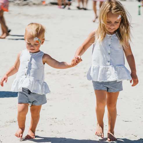 Two toddlers hold hands on the beach in matching outfits. Both of their faces are painted.