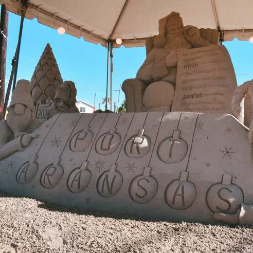 Sand sculpture of Santa's workshop. The focus is on a series of sand ornaments reading "Port Aransas."