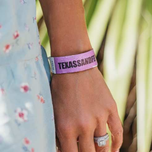 Close up on a woman's wrist that has a purple wristband on it reading "Texas SandFest"