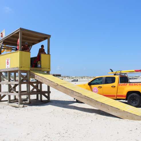 Lifegaurd towner with two lifegaurds in it. There is a beach rescue truck next to in parked in the sand.