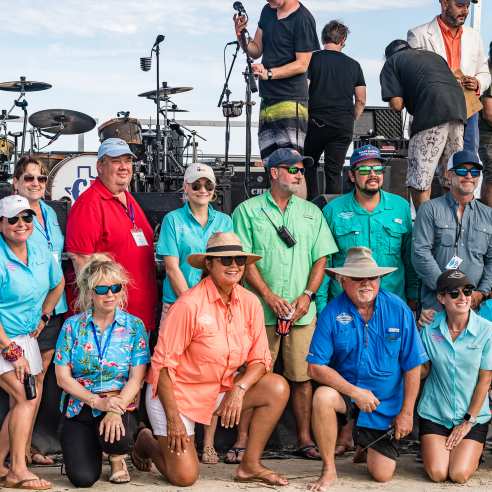 A group of people poses in front of a stage on the beach, smiling at the camera