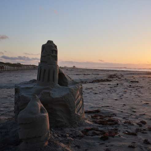 A sandcastle on the beach with the sun rising on the horizon