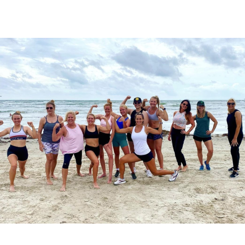 Group of women in workout clothes pose on beach
