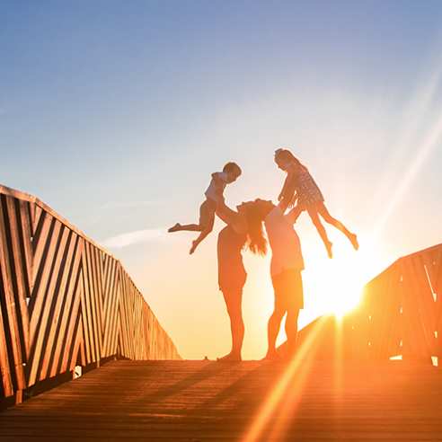 Parents lift their two children in the air on a boardwalk at sunrise in Port Aransas. Texas