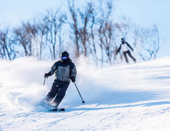 A skier carves down a snowy slope spraying snow behind.