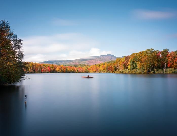 A kayaker is in the middle of a large mountain lake in autumn.