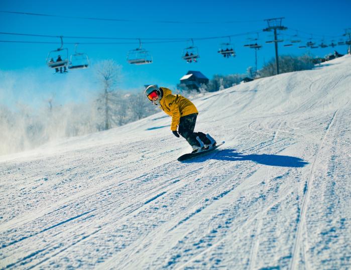 A snowboarder rides down the slopes at Beech Mountain Resort in a yellow coat and reflective goggles.