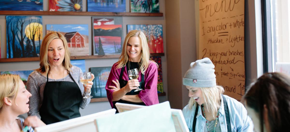 a group of women drinking wine and painting together