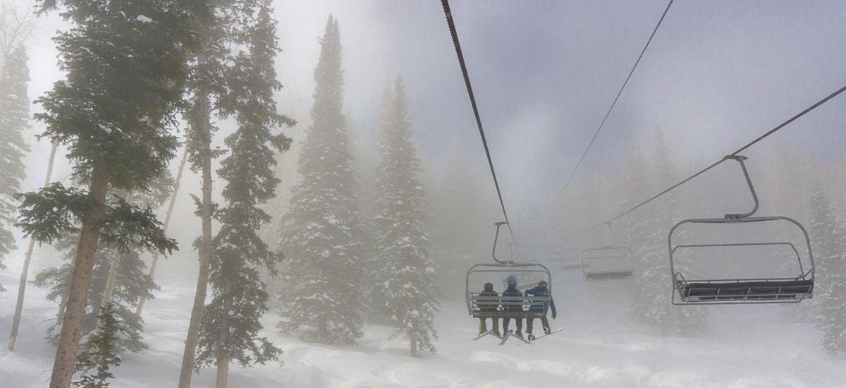 Three people riding up a chairlift through a cloudy morning
