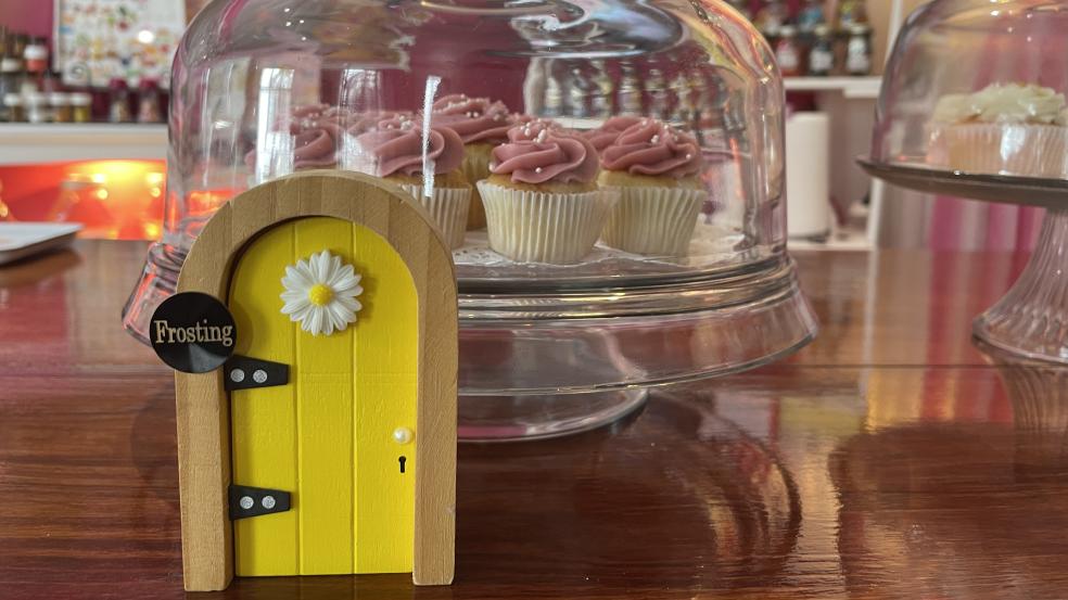 Yellow fairy door in front of cupcakes in a glass case at Our CupCakery