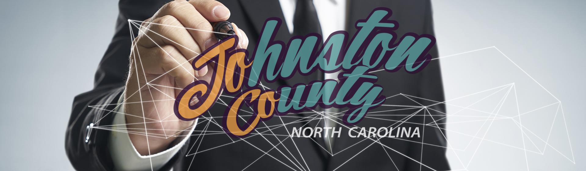 The Johnston County Visitors Bureau logo in front a hand drawing it.