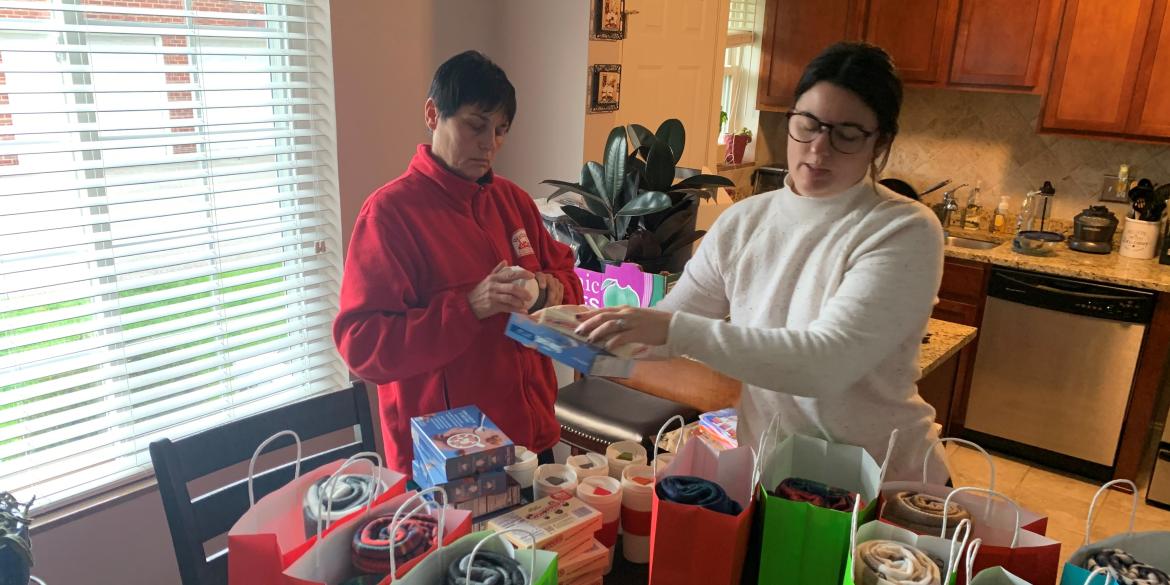 Two women pack holiday gift donations from home