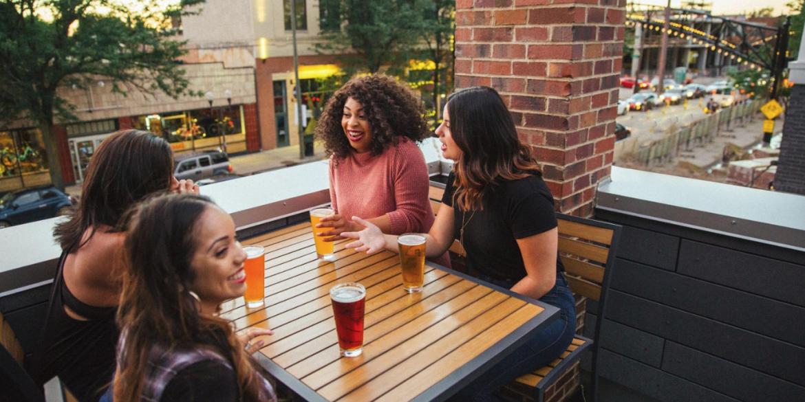Group of four women laughing and drinking beer on a rooftop patio
