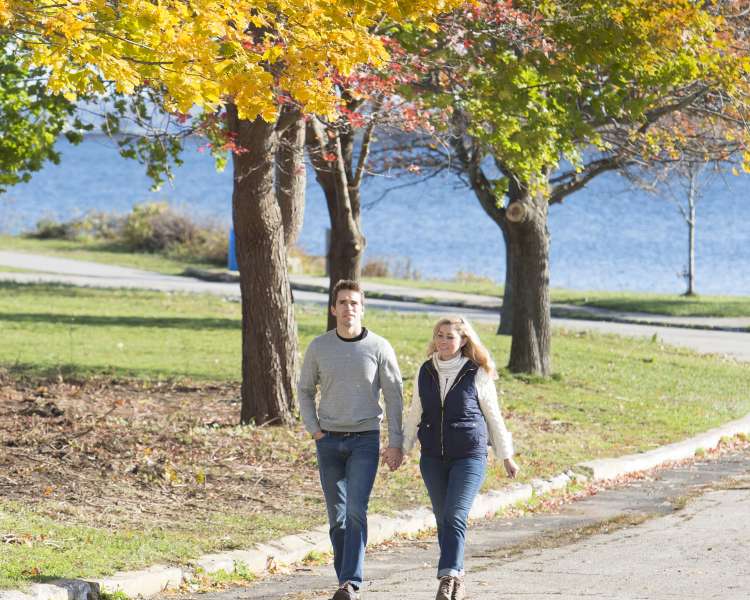 Man and woman walking through Rocky Point Park during autumn with waterfront in the background.