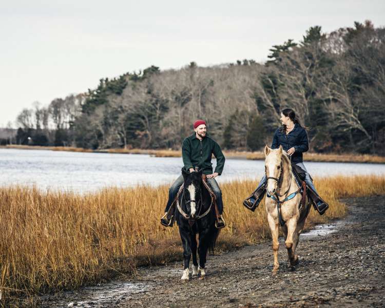 A man and woman riding horses along side the water