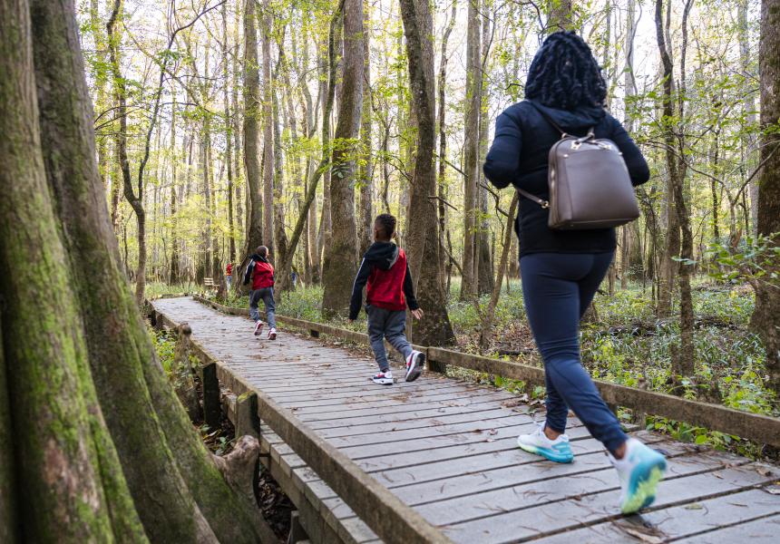 Two kids and a mother jog down a boardwalk through the woods