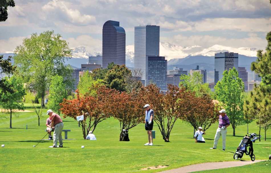 Golfers at City Park with Denver skyline and mountains.