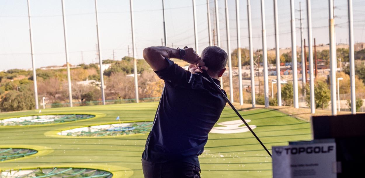 Man swinging club at topgolf during Thanks FORE Giving Golf Tournament hosted by the Visit Austin Foundation